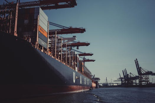 A large cargo ship docked at Hamburg Harbor, cranes loading containers under a clear sky.