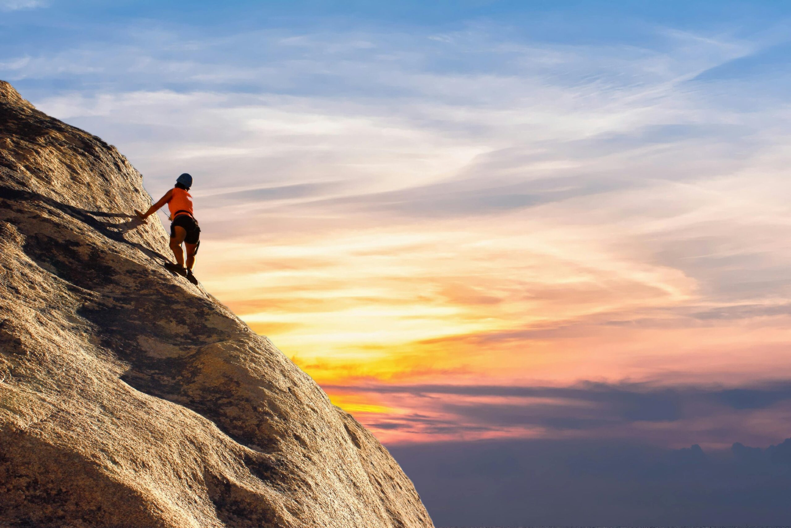 Climber conquers rock face at sunset, embracing the thrill and challenge.